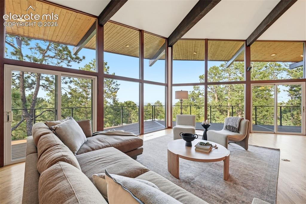 17 Pine Road Colorado Springs, CO 80906 - Photo 4 of 48 Living area featuring expansive floor-to-ceiling windows, wood-finish flooring, exposed ceiling beams, a wood-paneled ceiling, and glass sliding doors opening to an outdoor area