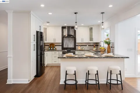 a kitchen with stainless steel appliances granite countertop a dining table chairs stove refrigerator and cabinets