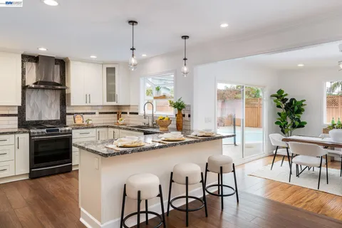 a kitchen with stainless steel appliances kitchen island granite countertop a stove a refrigerator a kitchen island a dining table and chairs with wooden floor