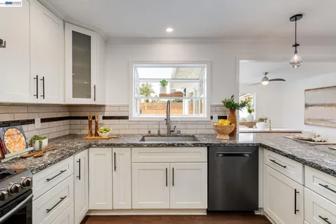 a kitchen with granite countertop a sink stainless steel appliances white cabinets and a window