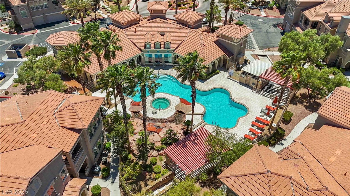 10550 West Alexander Road, Unit 2060 Las Vegas, NV 89129 - Photo 37 of 45 An inviting pool area with a spa nestles among buildings with warm-toned tile roofs, surrounded by lush palms.