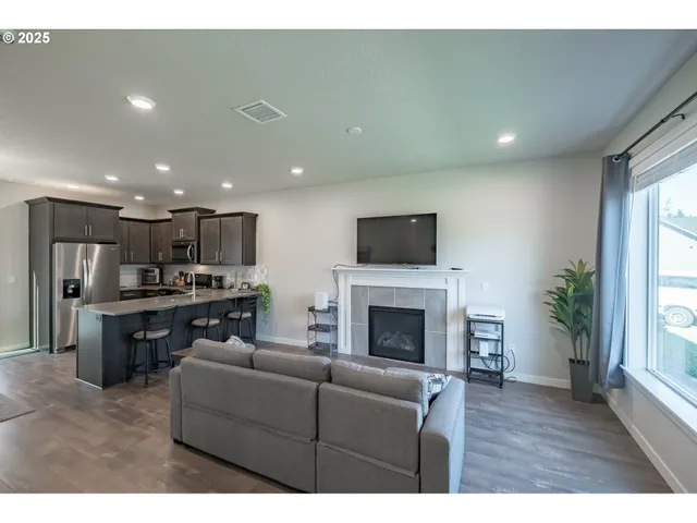 a living room with stainless steel appliances furniture a fireplace a flat screen tv and a window