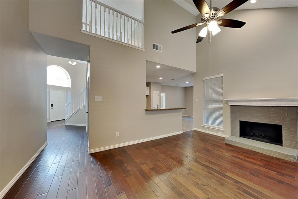 Unfurnished living room featuring dark wood-style flooring, a brick fireplace, a towering ceiling, a ceiling fan, and stairs