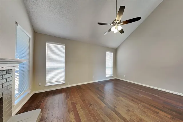 an empty room with wooden floor fan and windows