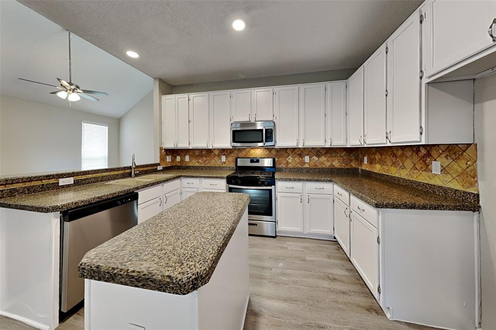 Kitchen featuring stainless steel appliances, white cabinetry, lofted ceiling, a peninsula, and a center island