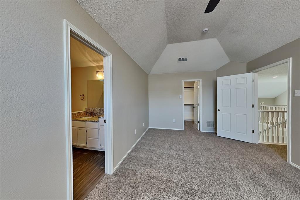 2301 Red Maple Road Flower Mound, TX 75022 - Photo 9 of 20 Unfurnished bedroom featuring a walk in closet, a textured ceiling, lofted ceiling, light carpet, and a ceiling fan