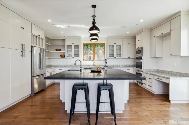 a kitchen with stainless steel appliances granite countertop a sink a stove a refrigerator and island with wooden floor