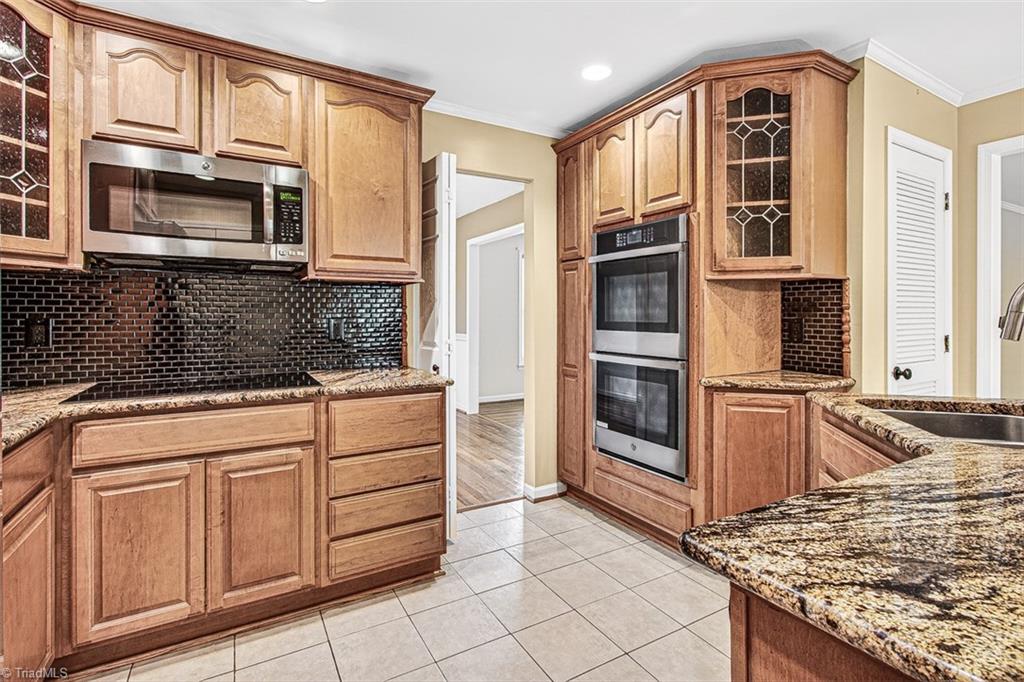 3903 Oakcliffe Road Greensboro, NC 27406 - Photo 11 of 42 Cabinets offer pull out drawers, decortive glass cabinets, granite counter tops and a ceramic tile back splash and an, induction cook-top.