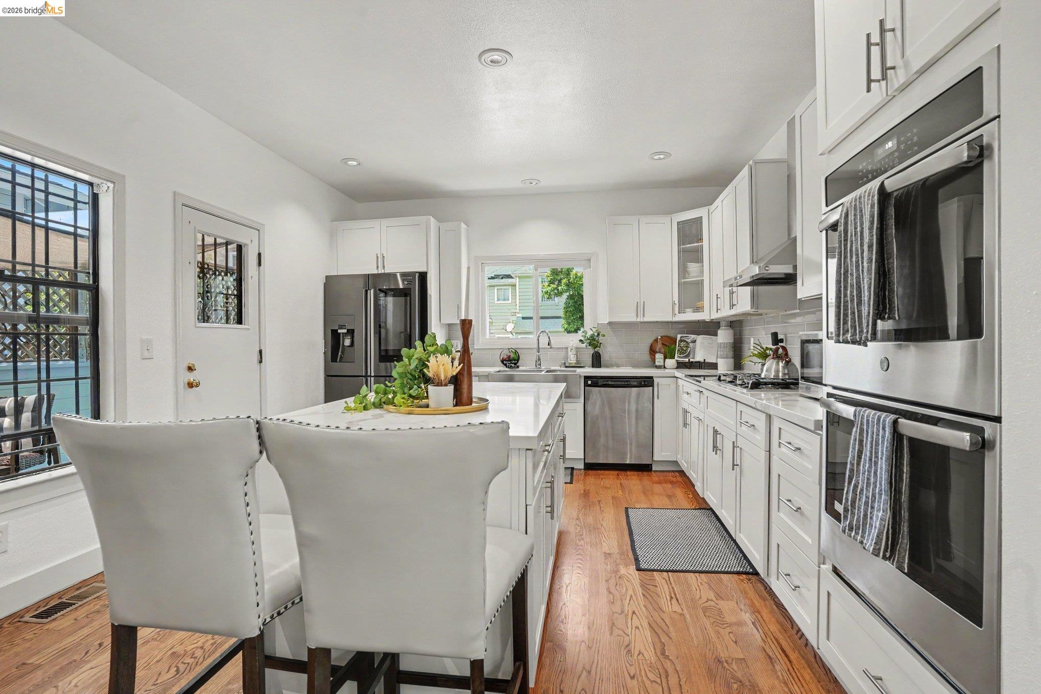 1433 Myrtle Street Oakland, CA 94607 - Photo 9 of 25 Open-concept kitchen featuring white cabinetry, stainless steel appliances, a center island with countertop seating, wood-finish flooring, and recessed lighting