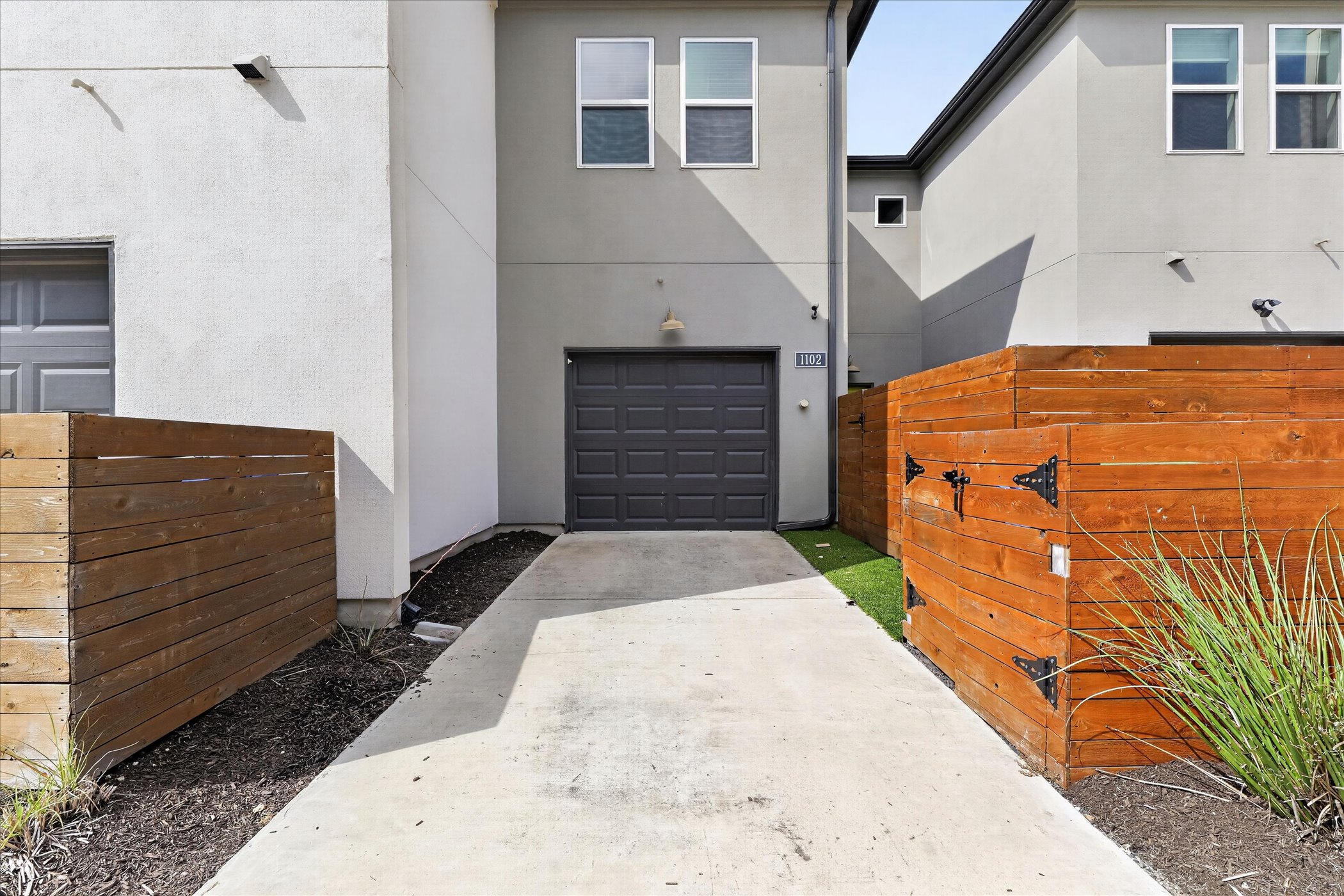 9015 Cattle Baron Path, Unit 1102 Austin, TX 78747 - Photo 23 of 25 A contemporary exterior showcasing a dark garage door and light-colored siding, accented by modern wood fencing.