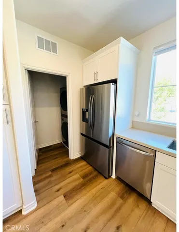 a view of a refrigerator in kitchen and an empty room with wooden floor