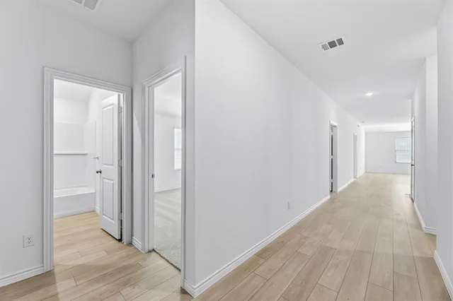 a view of a hallway with wooden floor and a bathroom