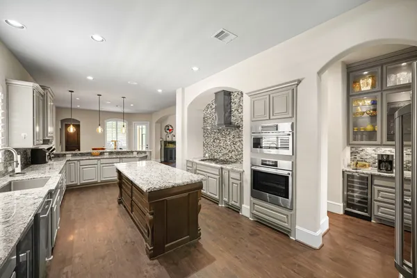 a kitchen with stainless steel appliances granite countertop a refrigerator oven a sink dishwasher and white cabinets with wooden floor