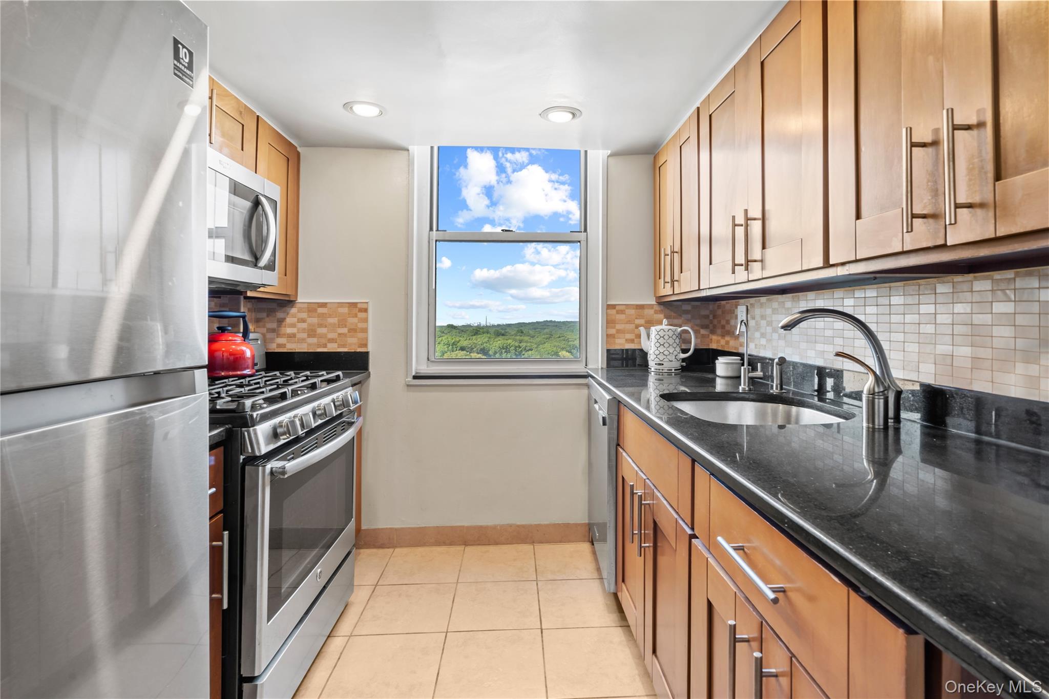 118-18 Union Turnpike, Unit 19G Queens, NY 11415 - Photo 6 of 16 Kitchen featuring appliances with stainless steel finishes, dark stone countertops, backsplash, brown cabinetry, and light tile patterned floors