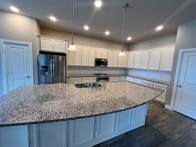 a large kitchen with stainless steel appliances a large counter top a sink and a wooden floor