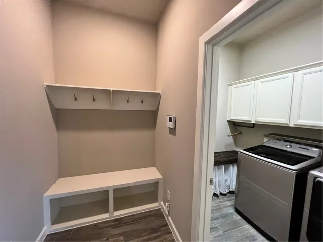 a view of an empty room with wooden floor and a kitchen