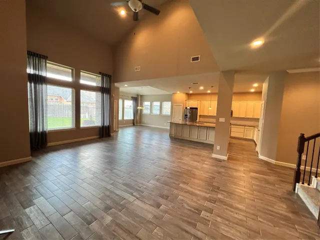 a view of an empty room with wooden floor and a kitchen