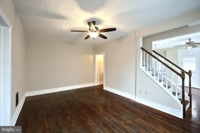 a view of an empty room with wooden floor and a ceiling fan