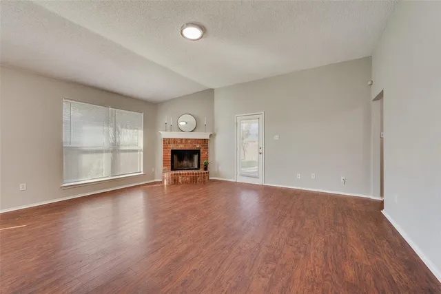 an empty room with wooden floor fire place and windows