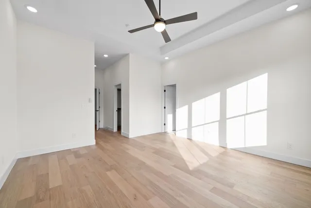 an empty room with wooden floor fan and windows