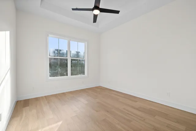 an empty room with wooden floor ceiling fan and windows