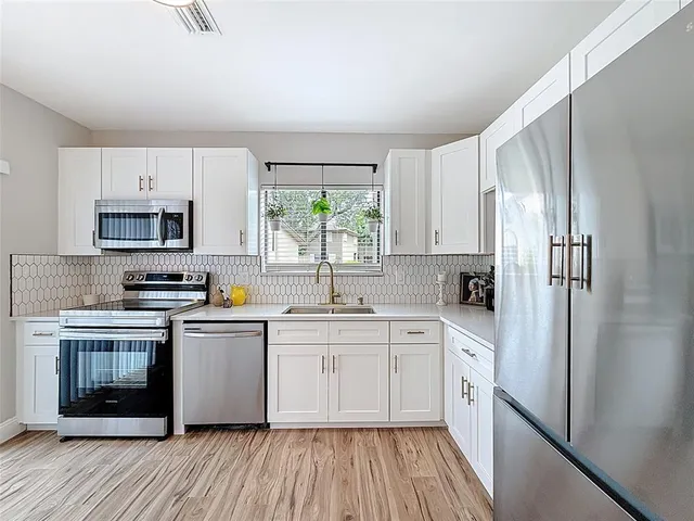 a kitchen with stainless steel appliances granite countertop a refrigerator a sink dishwasher a stove top oven a refrigerator with white cabinets and wooden floor