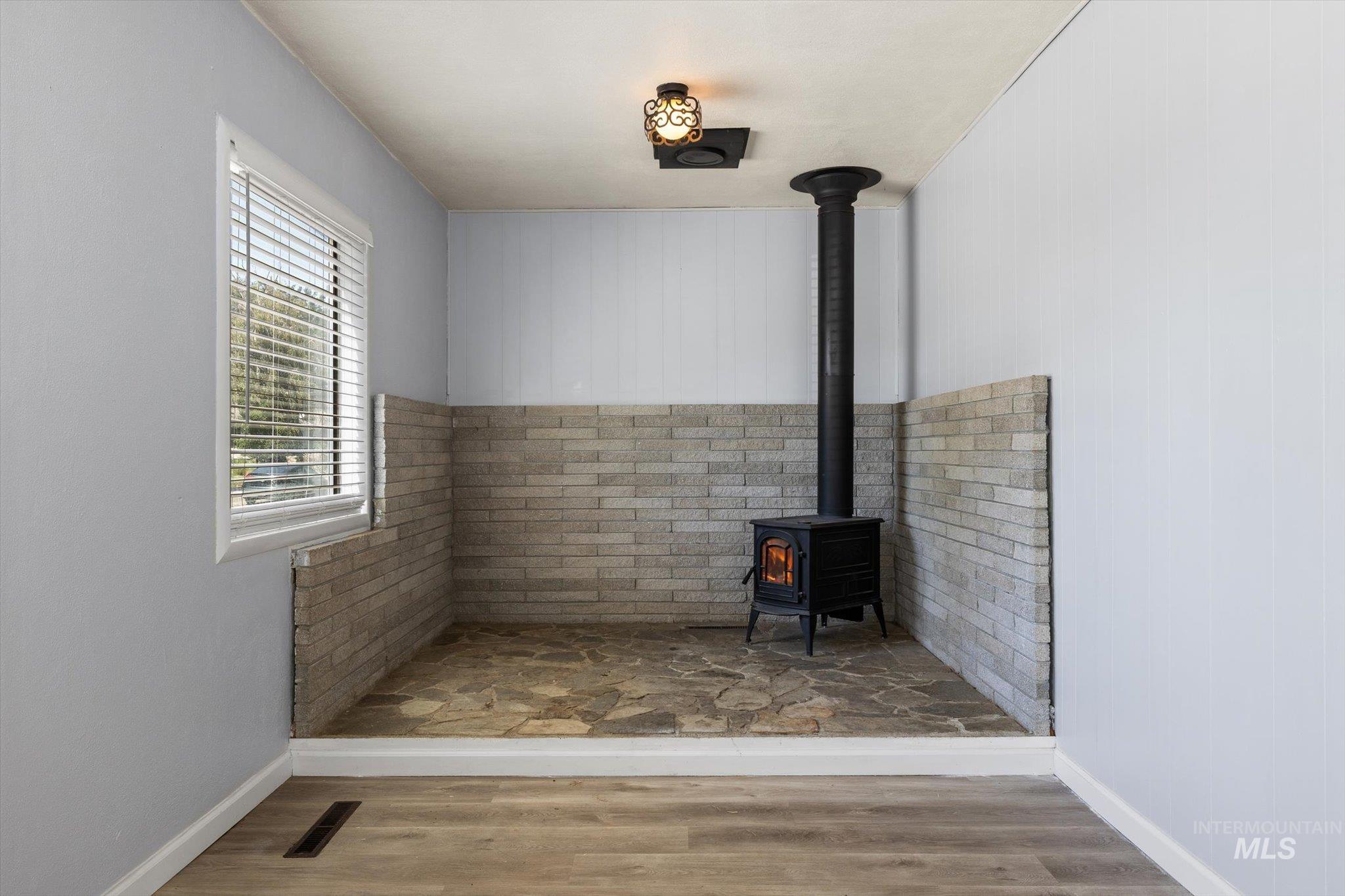 918 West 3rd Street Weiser, ID 83672 - Photo 9 of 36 Wood-burning stove with a black metal flue, set within a flagstone-style hearth and surrounded by a light-toned brick wainscoting