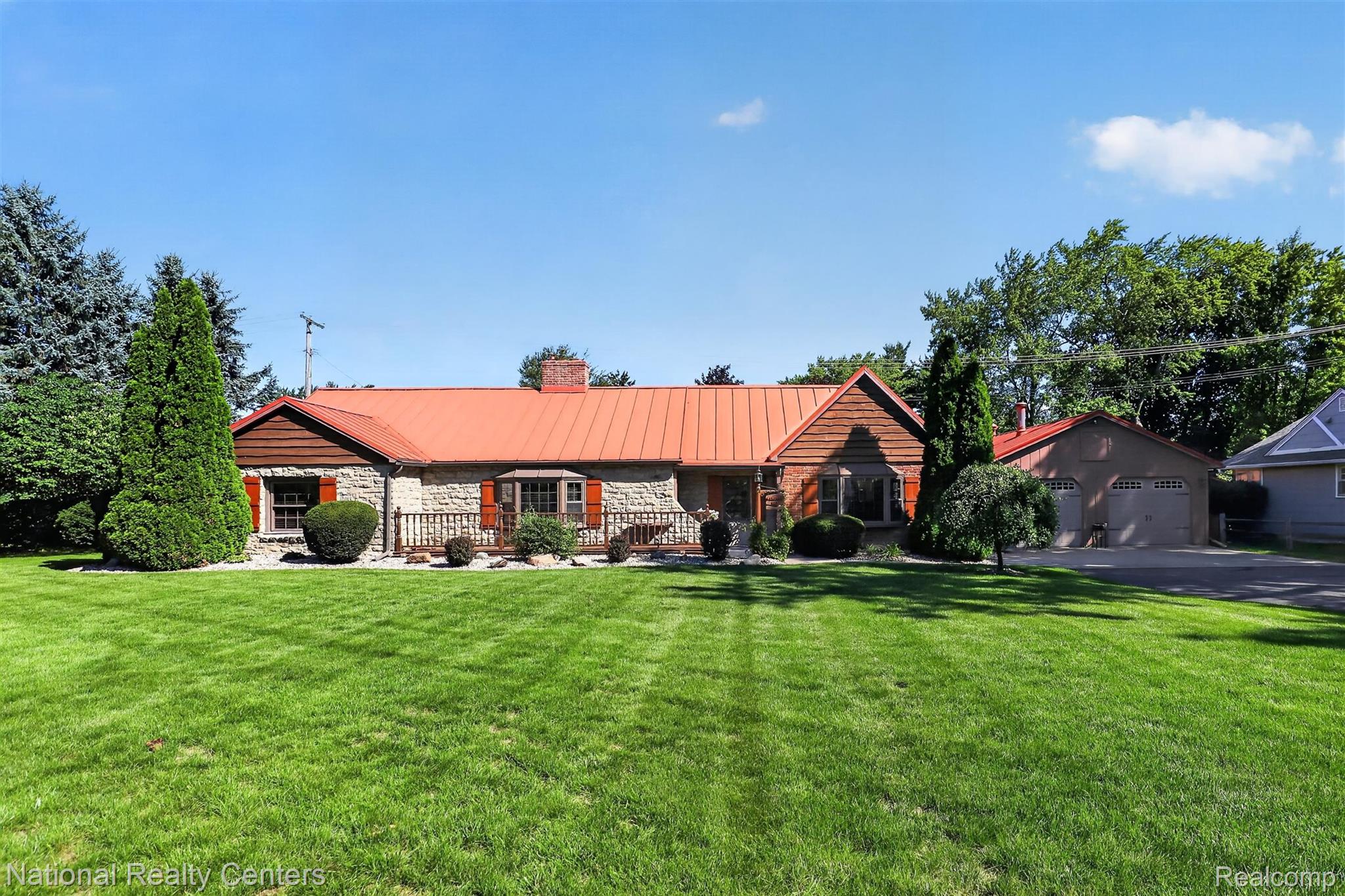 Stone facade with a prominent front porch, red metal roof, and a two-car garage