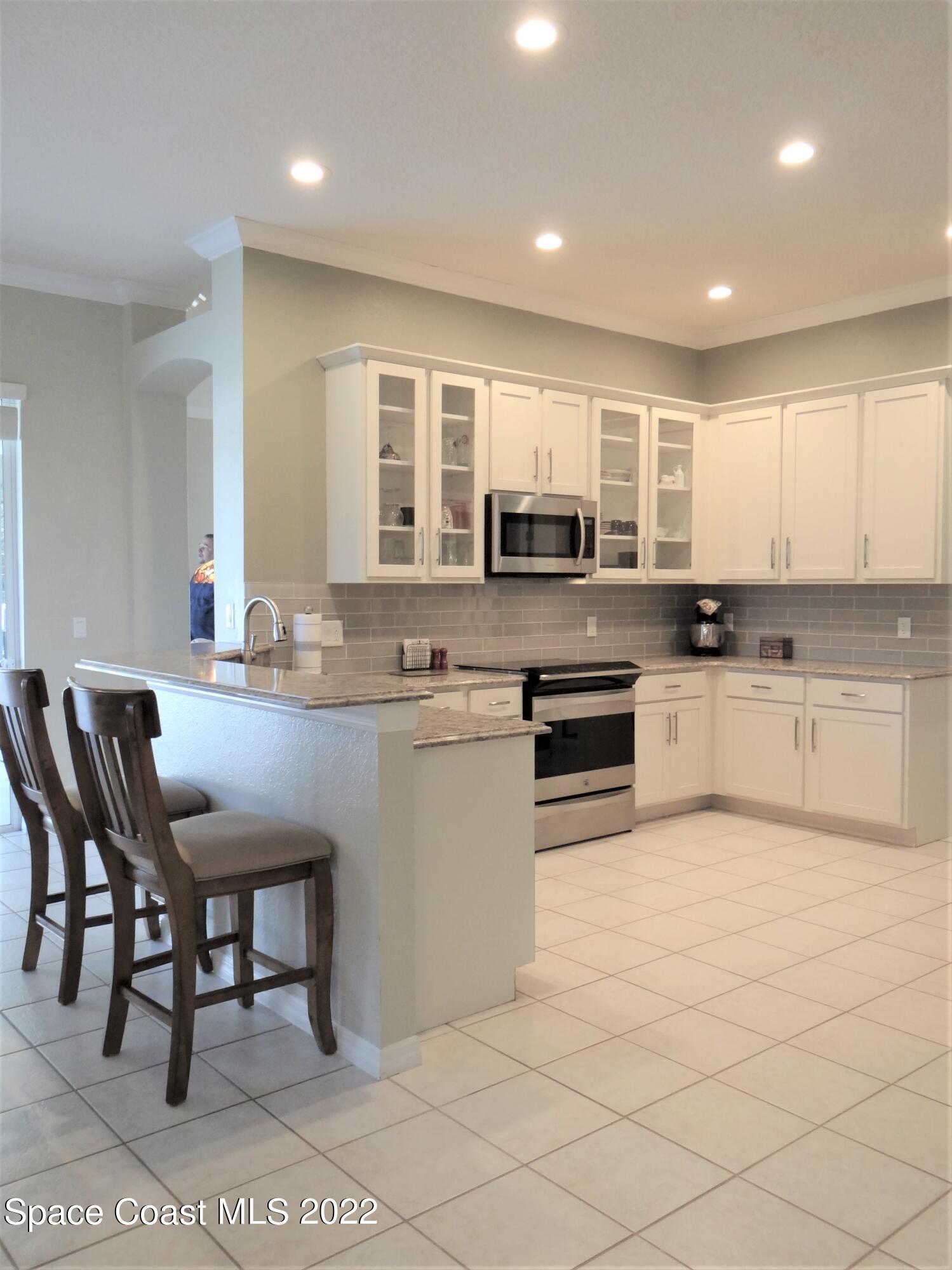 3100 Huntleigh Way Melbourne, FL 32934 - Photo 11 of 54 a kitchen with stainless steel appliances granite countertop a stove a sink a microwave a dining table and chairs