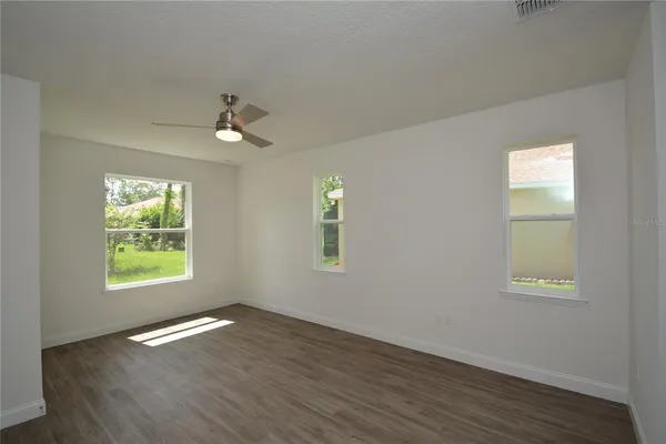 an empty room with wooden floor ceiling fan and windows