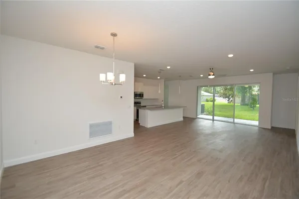 a view of an empty room with wooden floor and a kitchen