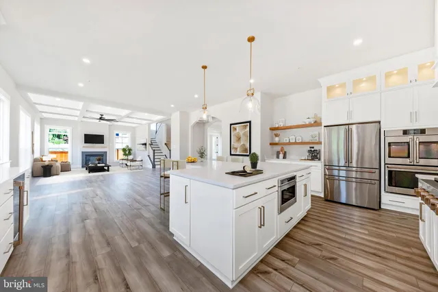 a kitchen with stainless steel appliances a stove top oven a refrigerator a sink and white cabinets with wooden floor