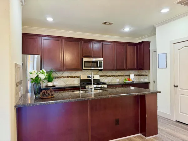 a kitchen with kitchen island granite countertop stainless steel appliances a sink a stove a microwave a refrigerator and cabinets