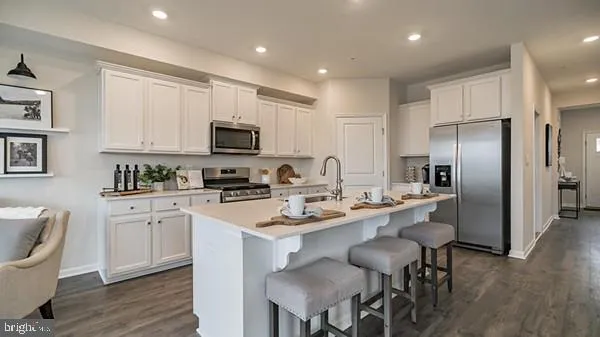 a kitchen with stainless steel appliances granite countertop a stove a sink a microwave a refrigerator and white cabinets with wooden floor
