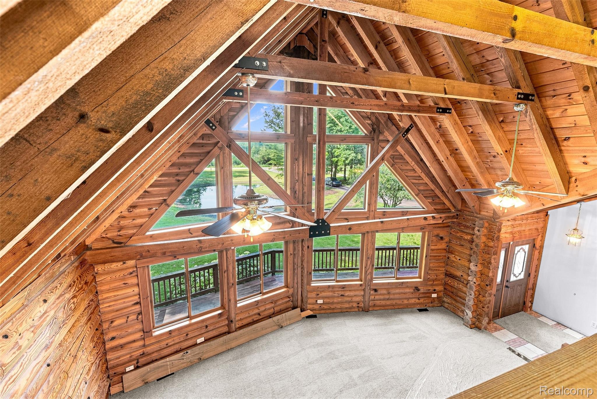 8340 North Nichols Road Flushing, MI 48433 - Photo 31 of 62 Vaulted exposed wood beam ceiling, large picture windows, wood-paneled walls, two ceiling fans with lighting, and a wood-finish entry door