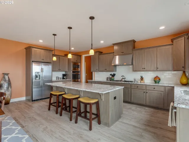 a kitchen with stainless steel appliances granite countertop a sink a stove a refrigerator and island with wooden floor
