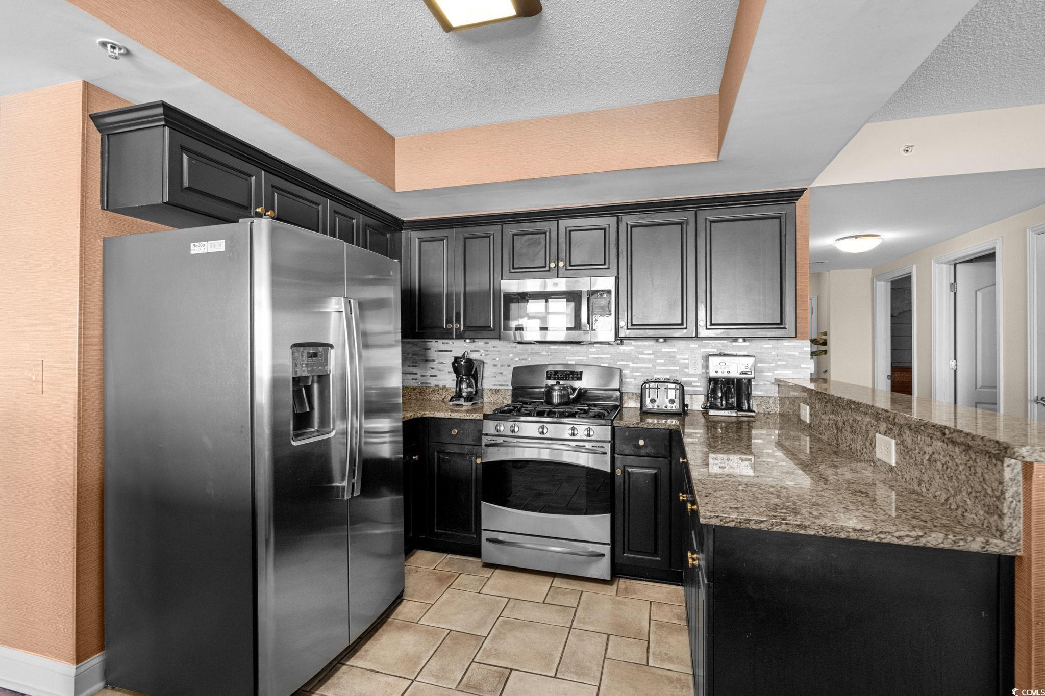 100 North Beach Boulevard, Unit 1803 North Myrtle Beach, SC 29582 - Photo 19 of 35 Kitchen with dark cabinetry, a raised ceiling, dark stone countertops, dishwasher, and hanging light fixtures