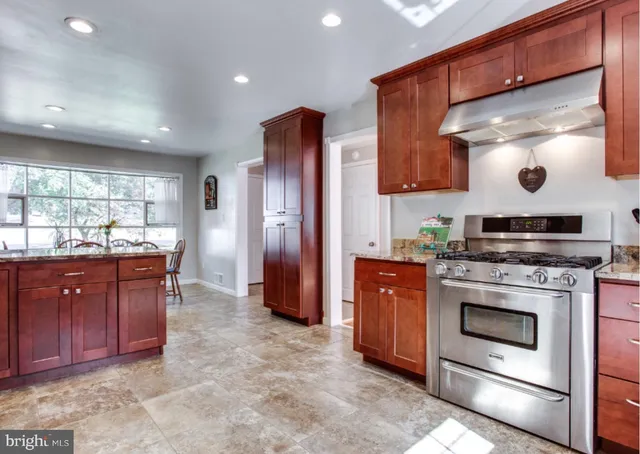 a kitchen with stainless steel appliances granite countertop wooden cabinets a stove a sink and a large window
