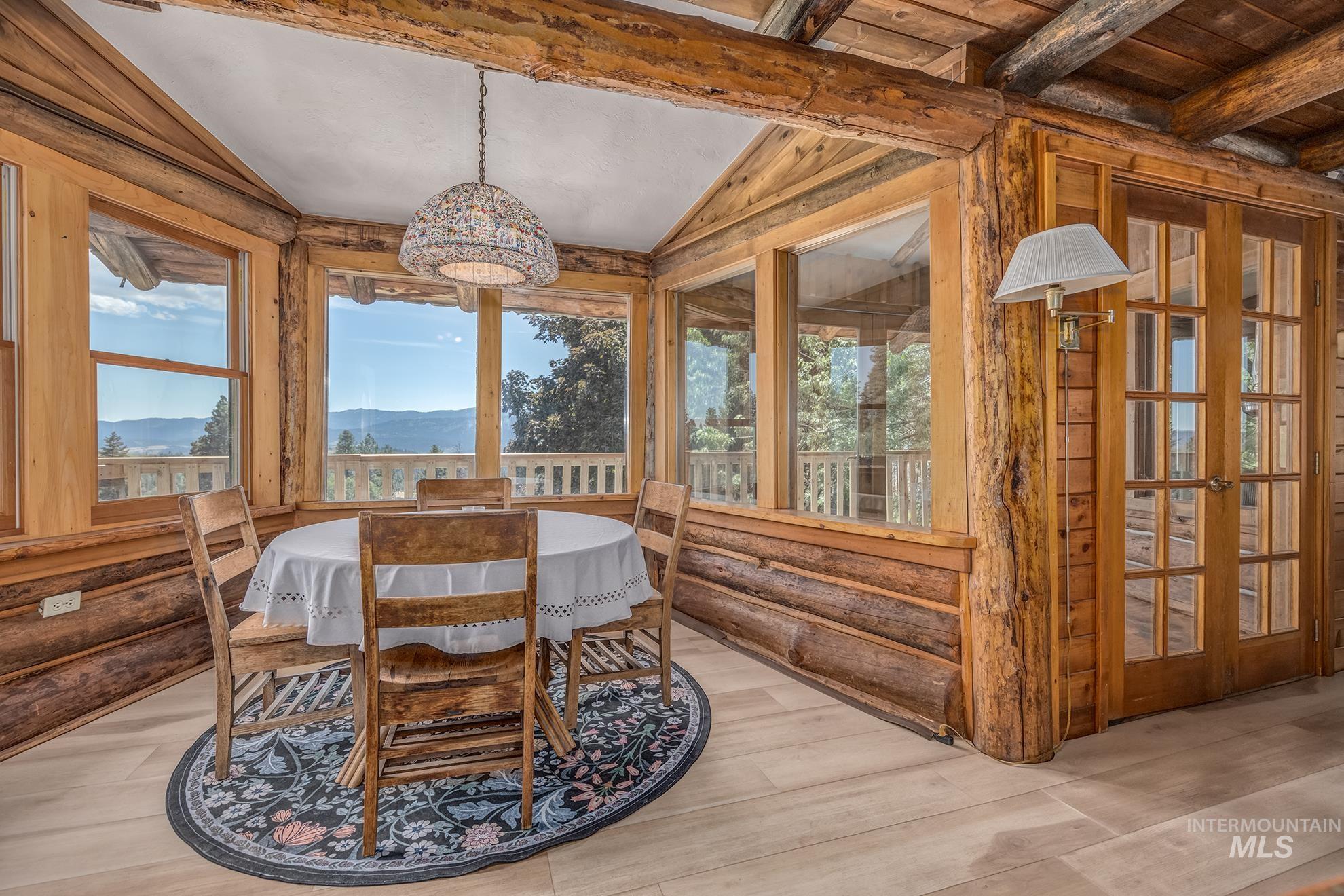 2150 Seid Creek Road Cambridge, ID 83610 - Photo 9 of 50 Sun-drenched dining area featuring natural wood walls and ceiling beams, expansive windows showcasing a mountain backdrop, and light wood-finish flooring