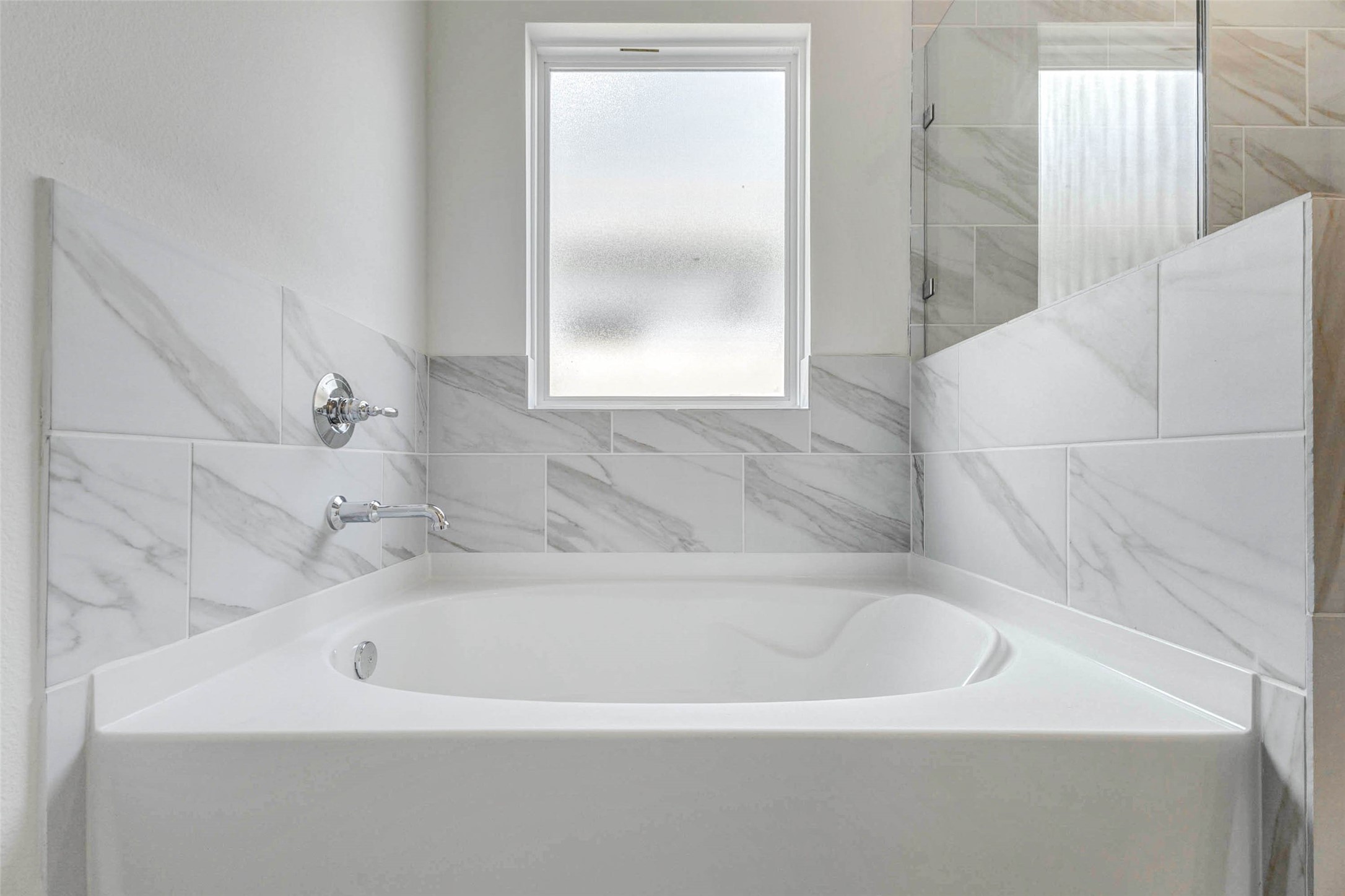 6463 Escondido Drive Rosharon, TX 77583 - Photo 25 of 30 Soaking tub in the primary bathroom surrounded by marble-look tile and a privacy window for soft natural light. This relaxing feature pairs beautifully with the separate shower to create a comfortable owner’s bath retreat.