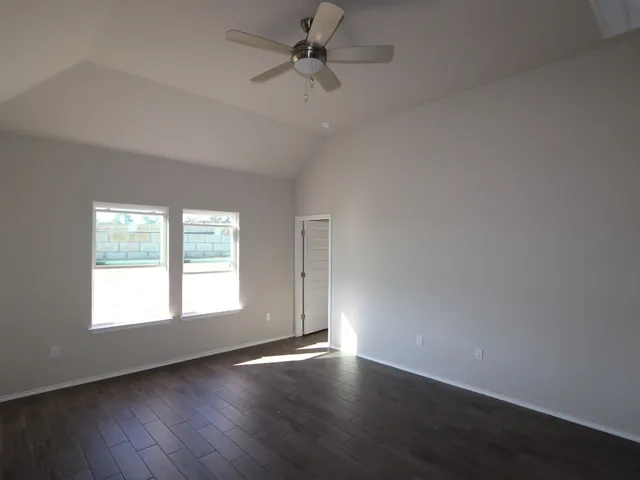 an empty room with wooden floor chandelier fan and windows