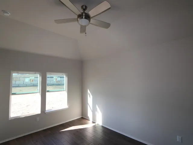 an empty room with wooden floor fan and windows