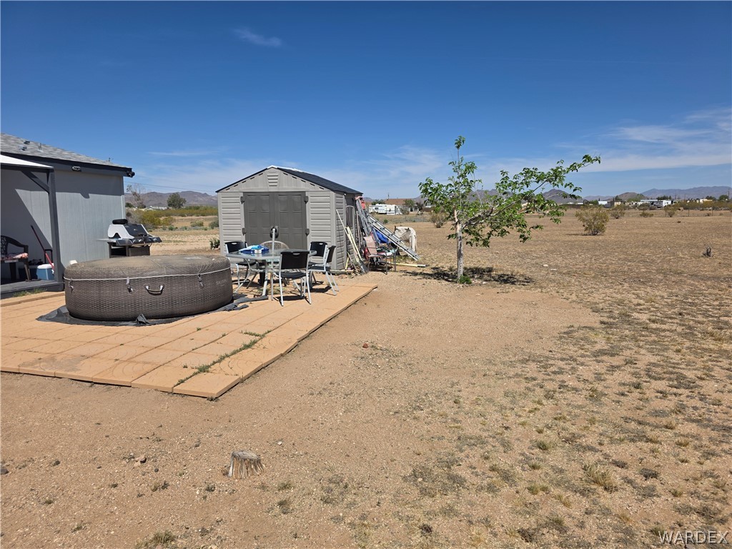 4182 Canelo Road Golden Valley, AZ 86413 - Photo 7 of 31 The property features a patio area with an outdoor spa, a storage shed, and a small tree, all set against a desert landscape
