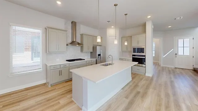 a large kitchen with kitchen island a stove a sink a refrigerator and white cabinets with wooden floor