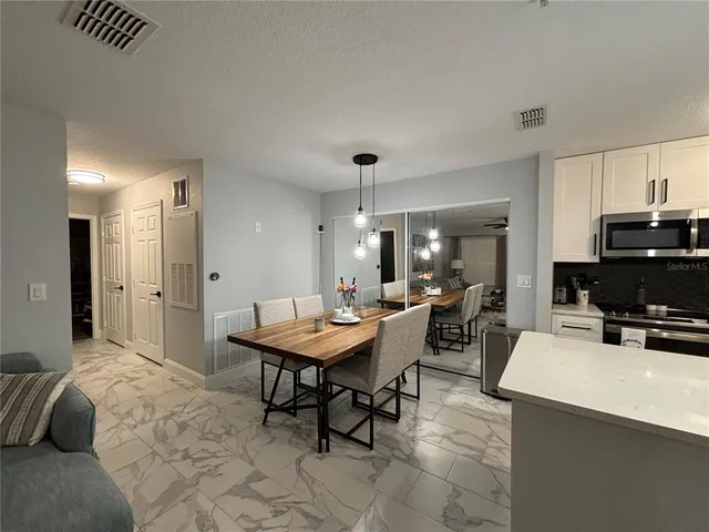 a kitchen with stainless steel appliances a sink dishwasher a refrigerator a stove a dining table and chairs with wooden floor