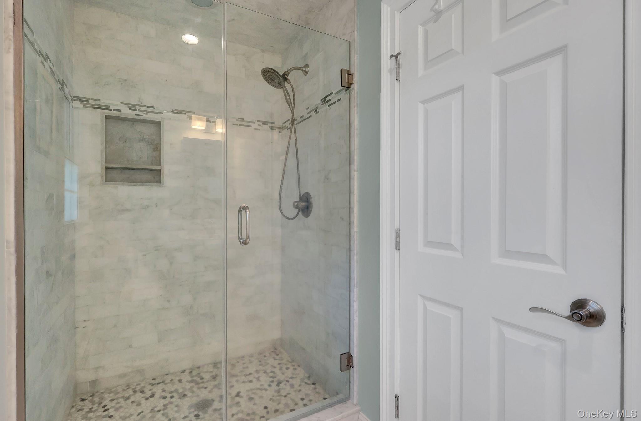24 Fox Road East Setauket, NY 11733 - Photo 26 of 48 Glass-enclosed shower featuring marble-look wall tiling, decorative mosaic accent tile, a recessed shower niche, and pebble-finish flooring