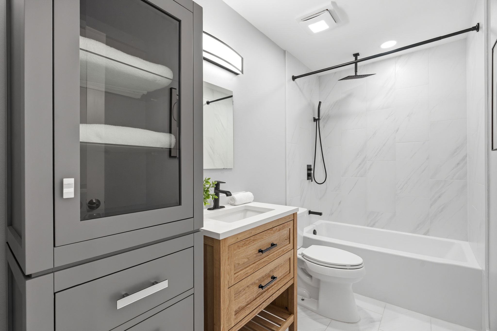 4802 Brighton Road Austin, TX 78745 - Photo 22 of 30 Stylish full bath features a wood-tone vanity, quartz countertop, modern black fixtures, a linen cabinet, and a tiled tub/shower surround extending to the ceiling.
