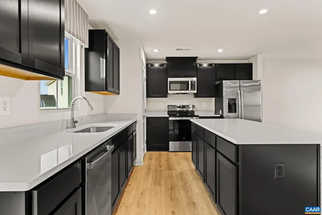 a kitchen with stainless steel appliances a sink dishwasher a refrigerator a stove top oven a refrigerator with wooden floor and cabinets