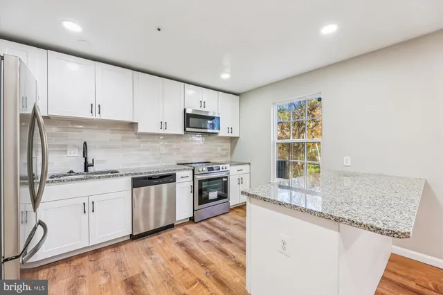 a kitchen with stainless steel appliances granite countertop a stove top oven a sink a refrigerator and white cabinets with wooden floor