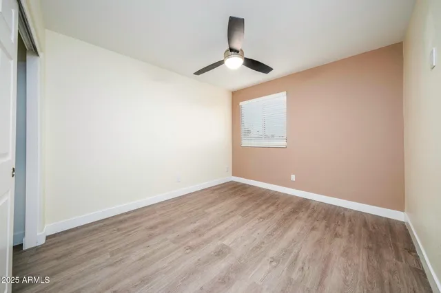 an empty room with wooden floor ceiling fan and windows